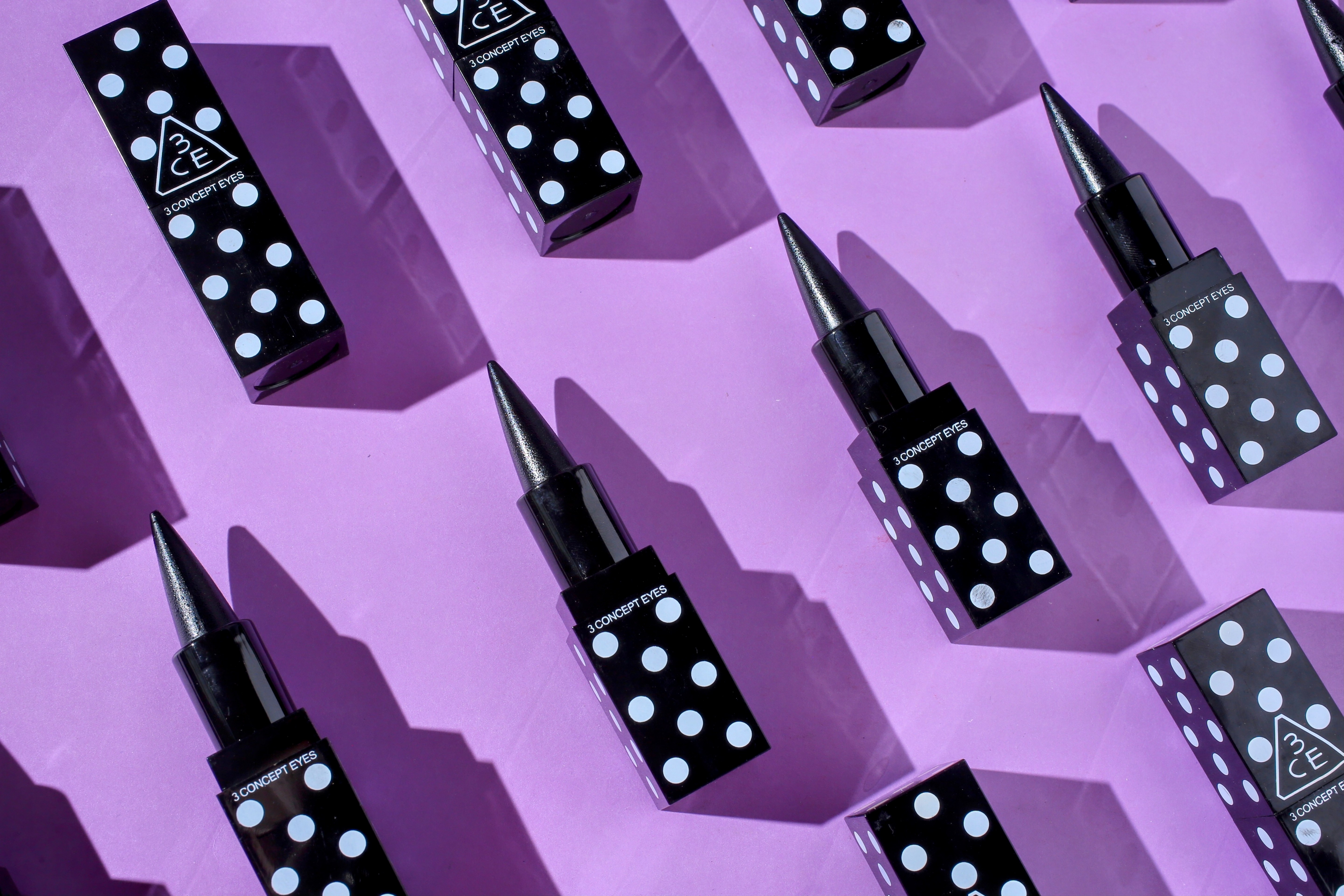 Multiple eyeliner products arranged in geometric flat lay on purple background